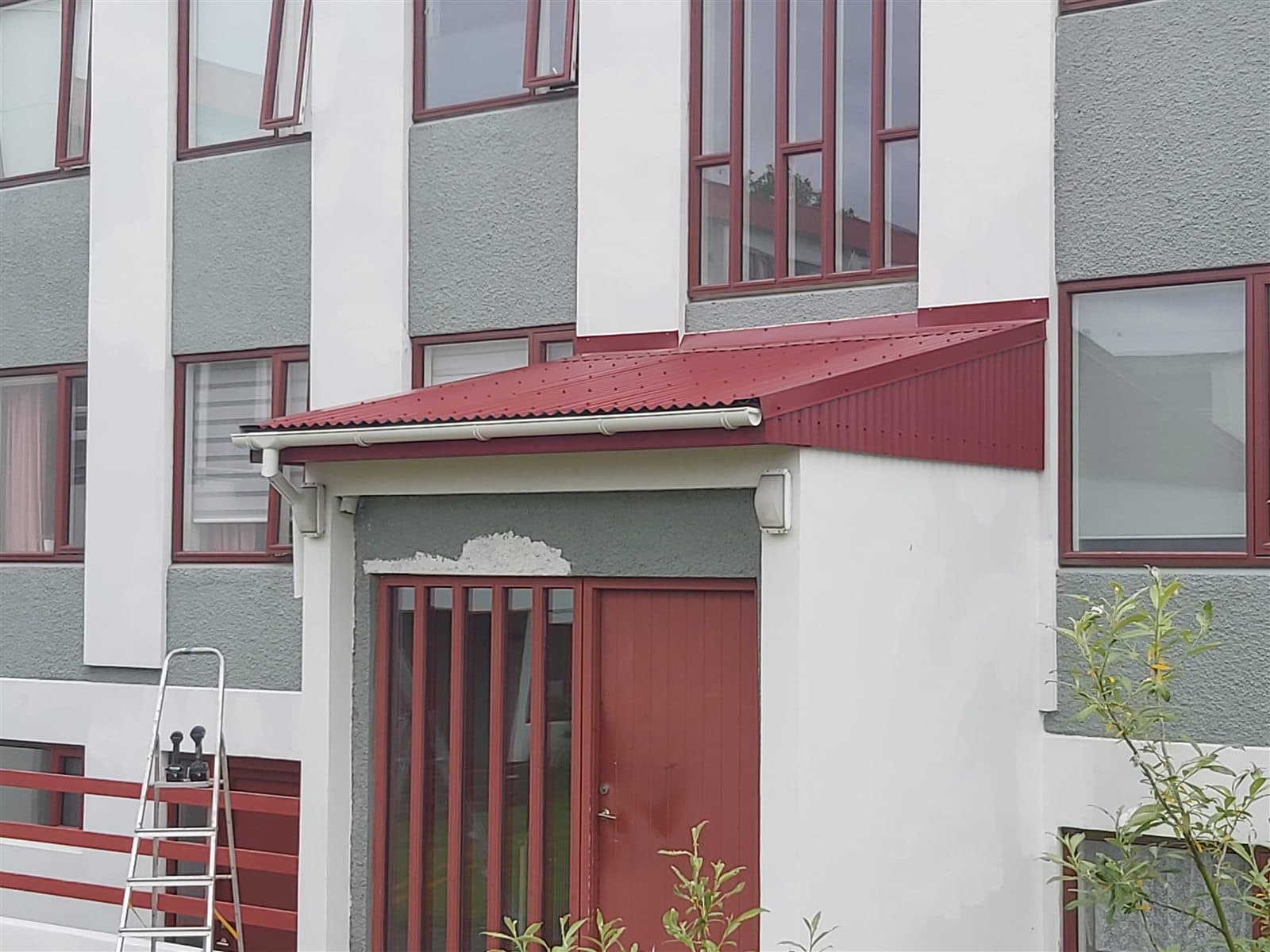 Nýtt einhalla þak með rauðri báruðri Greencoat klæðningu yfir inngangi fjölbýlis í Hólum, Breiðholti