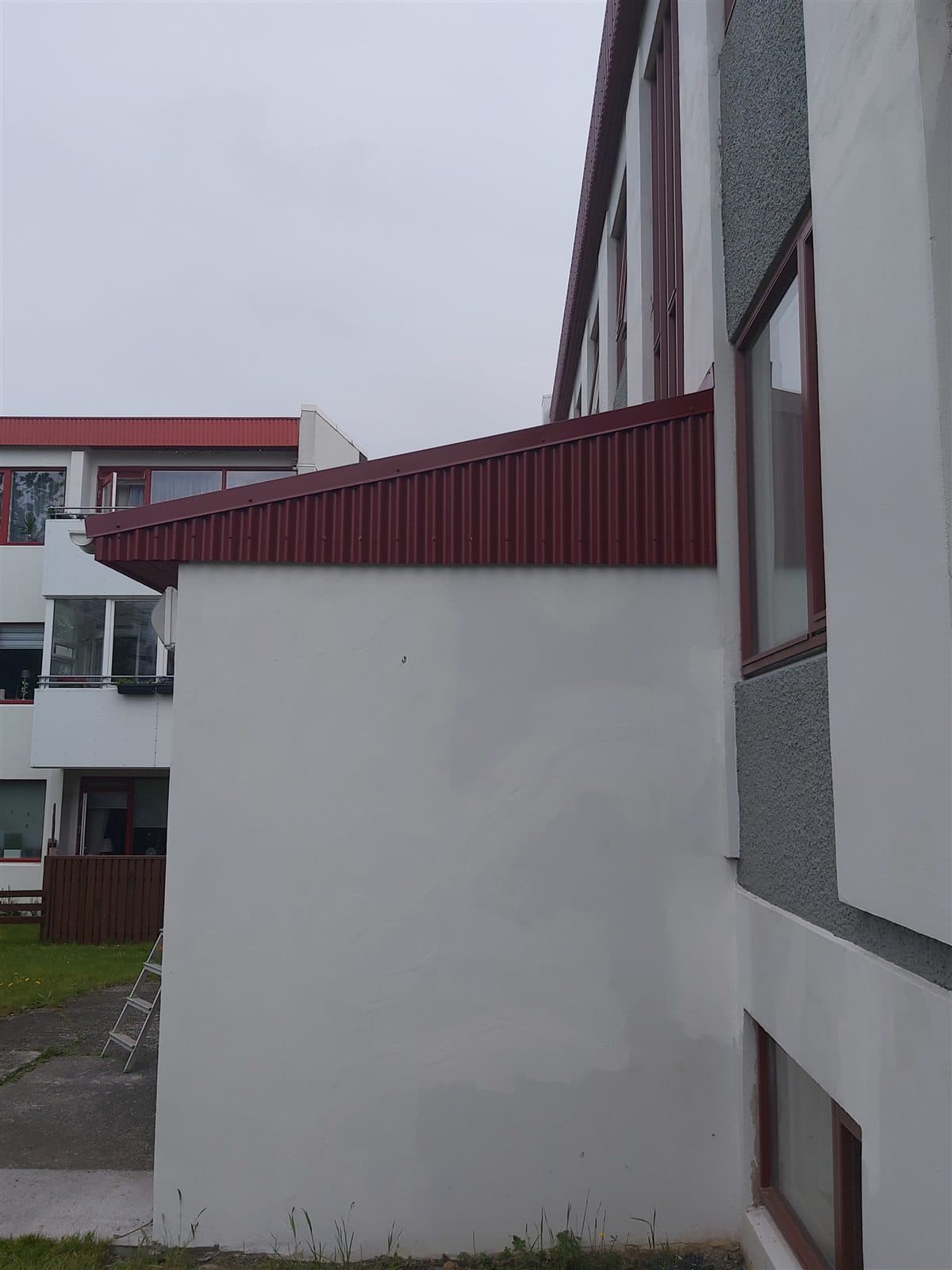 Einhalla þak sem leiðir vatn af inngangi fjölbýlis í Hólum — rauð báruð klæðning og flasningar